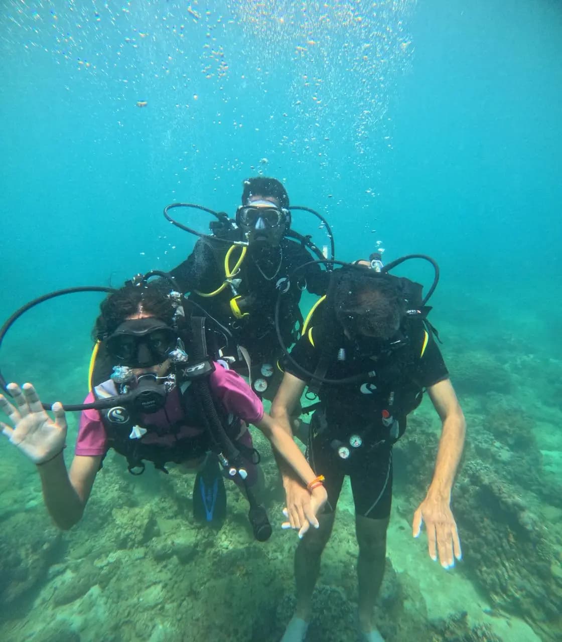 Three scuba divers waving underwater on a dive in Trincomalee, Sri Lanka