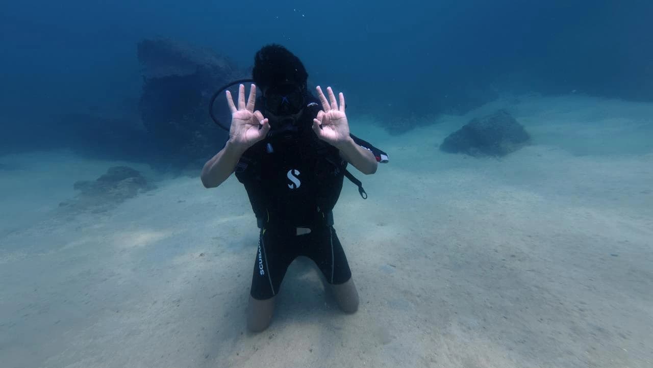 Scuba diver kneeling on the sand giving the OK signal underwater in Trincomalee